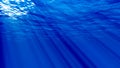 Dark blue ocean surface seen from underwater. Abstract waves underwater and rays of sunlight shining through. 3D Royalty Free Stock Photo