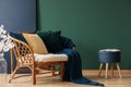 Dark blue pouf with open book next to rattan settee with pillows and blanket, copy space on the empty and blue grey wall Royalty Free Stock Photo