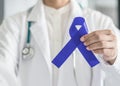 Dark blue ribbon for colon - colorectal cancer awareness on medical doctor`s hand support