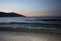 Dark blue sea waves over light sand with mountain and sunset on horizon