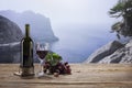 Dark bottle of red dry wine poured into glass, on wooden table isolated over mountain cliff landscape. Traditional Royalty Free Stock Photo