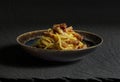 Dark bowl with spaghetti carbonara on black stone