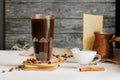 Dark brown coffee in tall glass mug on hot plate with coffee beans and cinnamon sticks, milk jug, Turkish coffee kettle on light Royalty Free Stock Photo