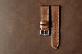 Dark brown leather watch strap with stainless buckle on leather background, Craft and handmade watch bracelet.