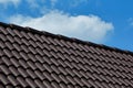 Dark brown modern ached clay tile sloped roof and ridge with blue sky and cloud