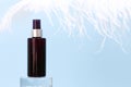 Dark brown spray bottle mockup on Glass podium and large white ostrich feather on blue background. Blank label bottle for branding