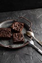 Dark cacao brownies with choco drops on old metal tray with vintage silverware on dark background