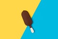 Dark chocolate dipped ice lolly on a yellow and light blue background