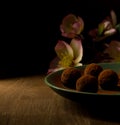 Dark chocolate truffles in green plate on wooden, and pink flowers in background. Royalty Free Stock Photo