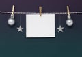Dark Christmas background with blank note paper, silver stars and baubles hanging from a string. With copy space