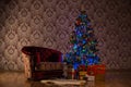 Dark Christmas scene with a lighted Christmas tree, gifts and armchair