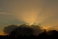 Dark clouds above silhouettes of bare winter trees, with rays of the hidden sun shining above Royalty Free Stock Photo