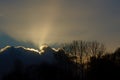 Dark clouds above silhouettes of bare winter trees, with rays of the hidden sun shining above Royalty Free Stock Photo