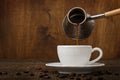Dark coffee pours from a copper jezve into a white cup Royalty Free Stock Photo