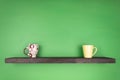 A dark color shelf with texturing wood is installed on a green wall; on the shelf there are two differently colored mugs Royalty Free Stock Photo