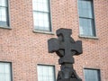 Dark concrete cross i focus. Red brick building out of focus in the background