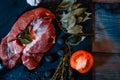 On a dark countertop, a large piece of raw beef, garnished with bay leaves, pepper