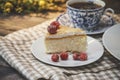 On a dark countertop on a light linen napkin on a white dish, a piece of cheesecake cake decorated with red berries, next to it is