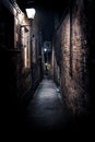 A dark creepy narrow European alley at night, surrounded by bricks and cobblestone. Illuminated only with some street Royalty Free Stock Photo