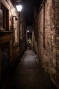 A dark creepy narrow European alley at night, surrounded by bricks and cobblestone. Illuminated only with some street Royalty Free Stock Photo