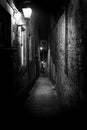 A dark creepy narrow European alley at night, surrounded by bricks and cobblestone. Illuminated only with some street lamps. Royalty Free Stock Photo