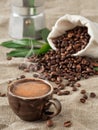 Dark cup of coffee with smoke espresso and coffee beans in burlap sack on a burlap background. Close up, soft focus. Near coffee