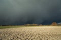 Dark dangerous cloud coming over a plowed field, forest on the horizon