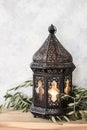 Dark decorative Moroccan lantern. Green olive leaves, branches on old wooden table. Selective focus, shabby wall