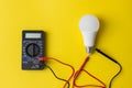 Dark Digital multimeter with probes and LED bulb on yellow background. Power saving concept. A multimeter is an electronic Royalty Free Stock Photo