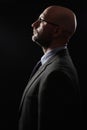 Dark dramatic portrait of a bald slim businessman in grey suit, blue shirt, tie and glasses. Royalty Free Stock Photo