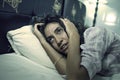 Dark and edgy portrait of depressed and sleepless latin woman lying worried and awake on bed at night suffering insomnia and