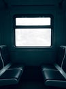Dark empty cabin of a passenger train car with seats and a window in the center behind which is a white sky