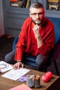 Dark-eyed astrologist wearing red cardigan sitting at the table with candles