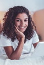 Dark-eyed curly girl smiling while watching photos