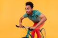 Dark-eyed young man in green t-shirt riding on bike on yellow background. Happy african guy in casu