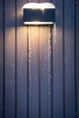 Dark, frozen house wall with icicles and street light background. Old, grey, vertical wooden boards with shine. Winter holidays