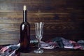 Dark glass wine bottle without label, empty transparent wineglass and colored cloth on brown wooden board background. Royalty Free Stock Photo