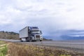 Dark gray big rig semi truck with powerful grille guard transporting cargo in dry van semi trailer running on the road with sky Royalty Free Stock Photo