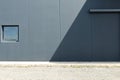 Dark gray concrete block wall divided in two by shadow. Cement sidewalk and asphalt road in front