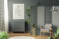 Dark, gray living room interior with a sketch hanging above a wooden chest of drawers next to a screen, golden table and armchair