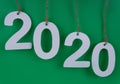 on a dark green background, numbers twenty twenty white on new year date hang from top to bottom on brown ropes