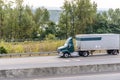 Dark green big rig day cab semi truck transporting cargo in short semi trailer driving on the divider road Royalty Free Stock Photo