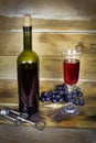 Dark green bottle and transparent wineglass with red wine and bunch of grapes on wooden plank surface, corkscrew nearby Royalty Free Stock Photo