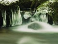 Dark green cold water of mountain stream in winter time, small icicles are hanging Royalty Free Stock Photo