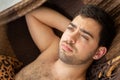 Dark haired bare chested unshaven young man resting in a brown hammock