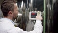 A dark-haired bearded labouring man is setting up parameters for a factory equipment. A slow motion close up shot from