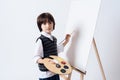 The dark-haired boy draws on the easel. He holds the paint and brush in his hand.