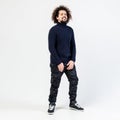 Dark-haired curly guy with a beard in a black turtleneck, khaki pants and sneakers poses in the studio on the white