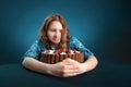 Dark-haired girl on a diet looks at a chocolate cake, struggling with the desire to eat it