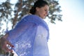 Horizontal closeup photo of a beautiful brunette in a lilac shawl against a background of pines and a winter sky Royalty Free Stock Photo